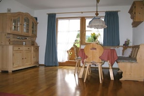 Een kamer met een houten kast, een eettafel met stoelen, een bankje en een raam met gordijnen.