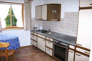 A kitchen with a sink, stove, and cabinets. There is a window with curtains and a view of greenery outside. - Holiday apartment with 1 bedroom (Garmisch-Partenkirchen)