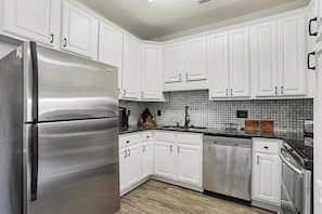 A modern kitchen with white cabinetry, a stainless steel refrigerator, and a tiled backsplash. - Salt and Sand Myrtle Retreat (North Myrtle Beach)