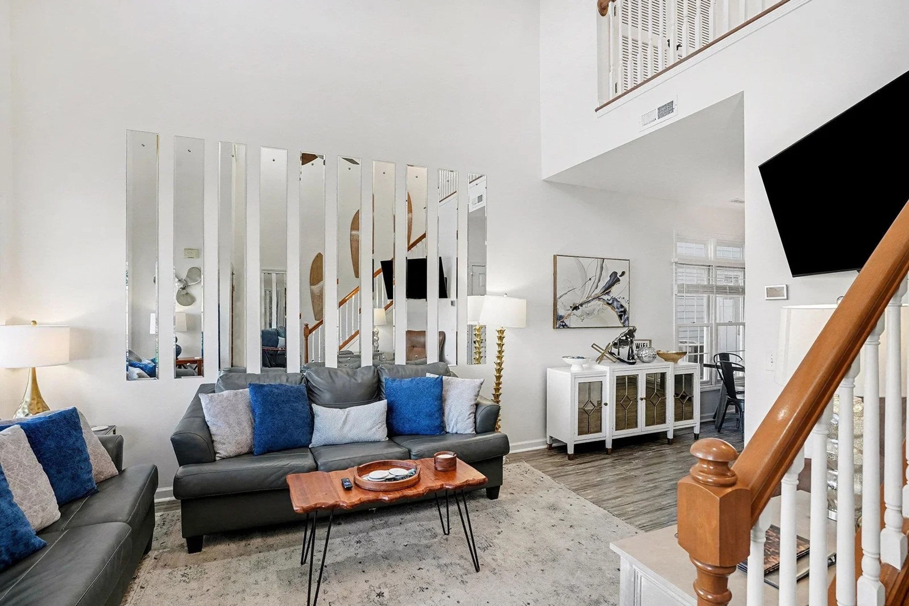 A modern living room with a grey sofa, a coffee table, and a large mirror.