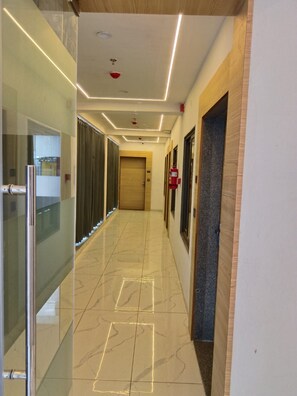 Un pasillo con una puerta de cristal a la izquierda, un extintor a la derecha y una puerta de madera al final.