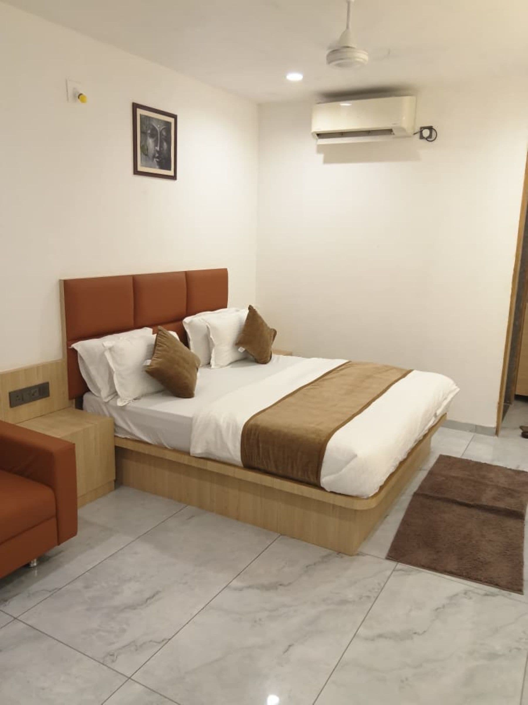 A bedroom with a bed, bedside tables, a chair, a picture on the wall, and an air conditioning unit.