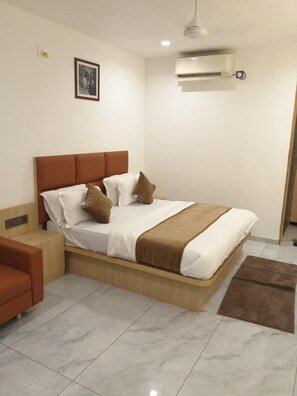 Un dormitorio con cama, mesitas de noche, una silla, un cuadro en la pared y un equipo de aire acondicionado.