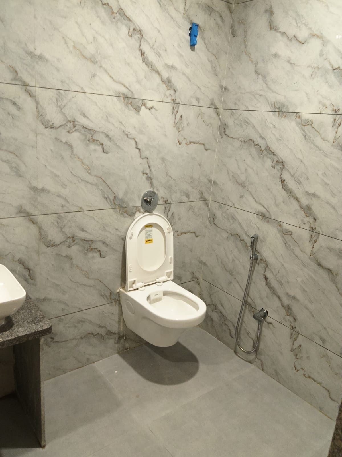 Un baño con pared de mármol, inodoro blanco y ducha.