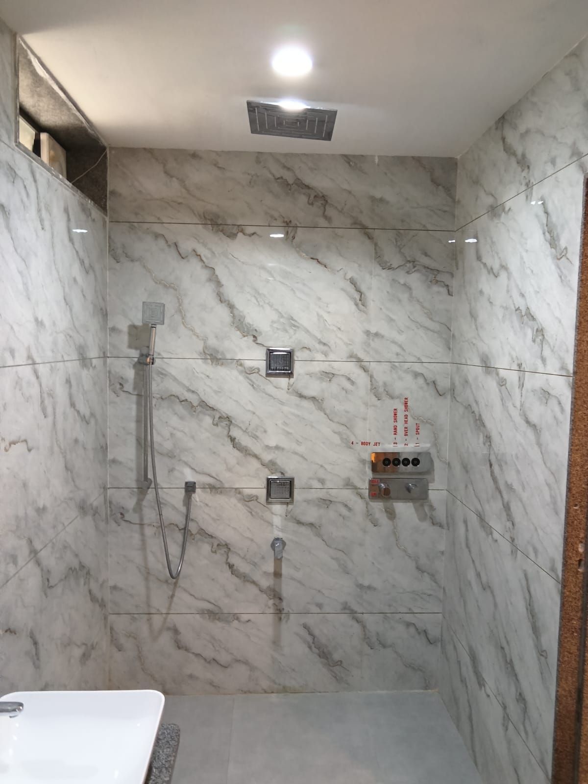 A modern bathroom with a marble wall, a shower with a handheld showerhead, and a control panel for water temperature and flow.