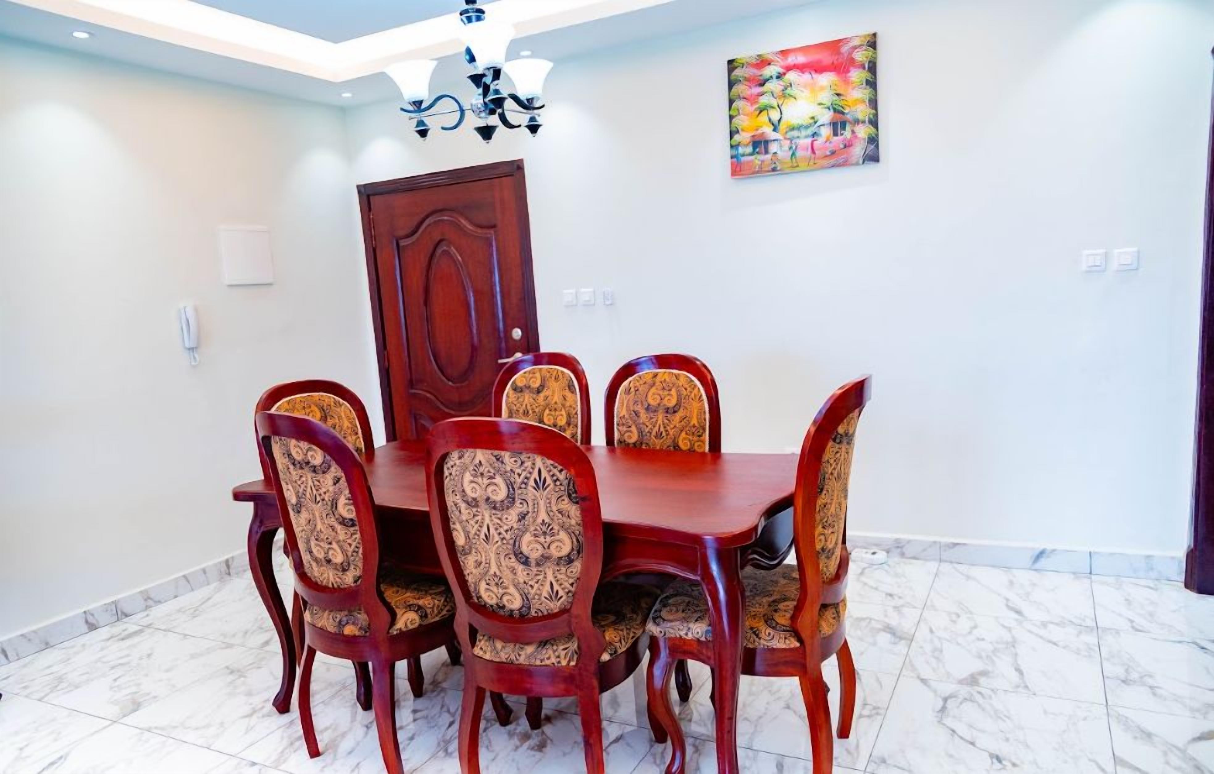 A dining area with a wooden table and chairs, a chandelier, a door, and a colorful painting on the wall.