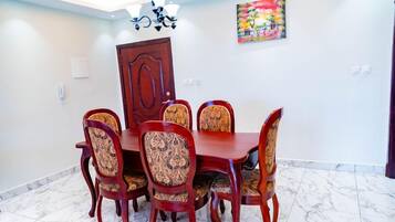 A dining area with a wooden table and chairs, a chandelier, a door, and a colorful painting on the wall.