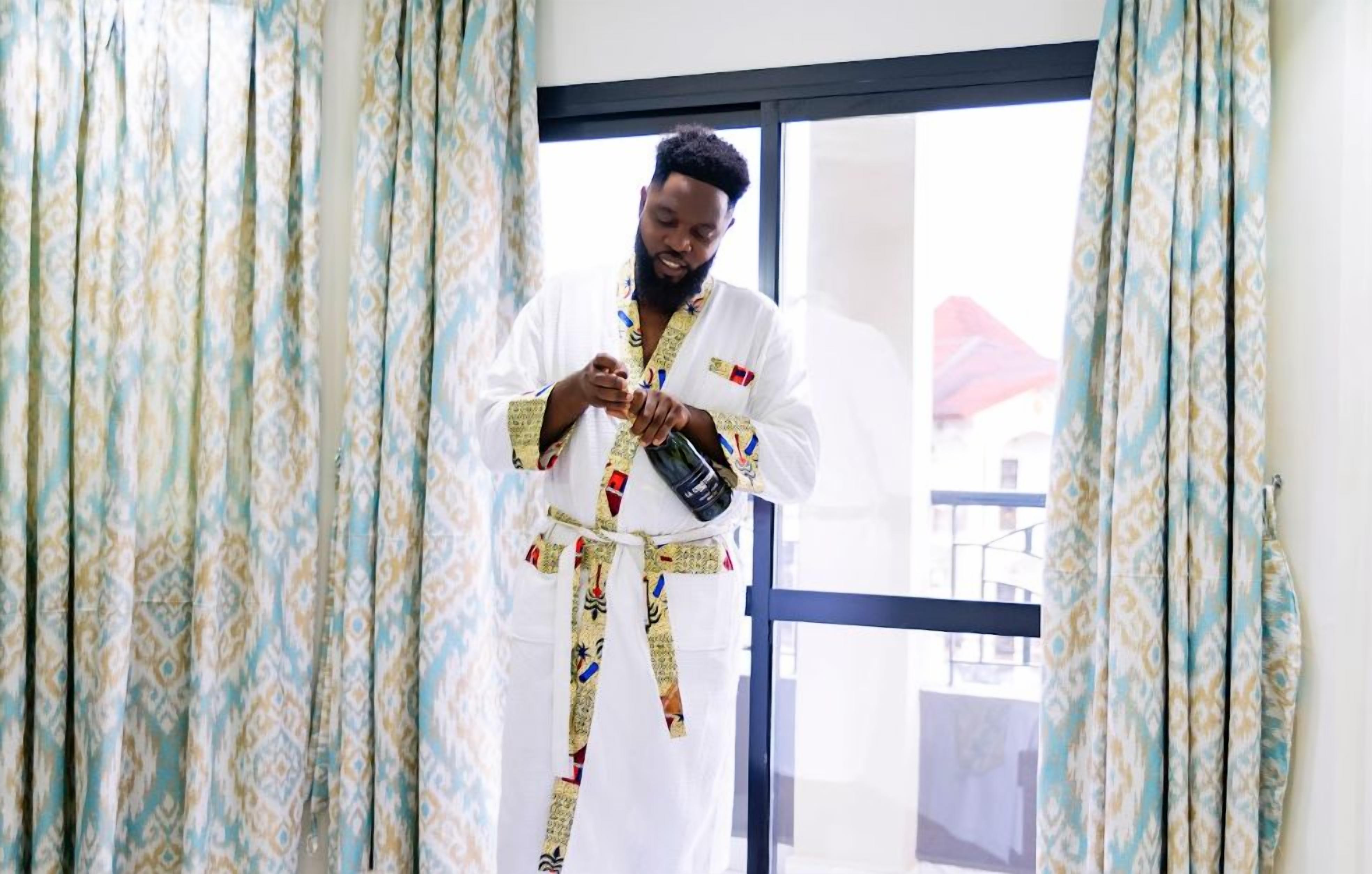A person standing in a doorway with patterned curtains, holding a bottle.