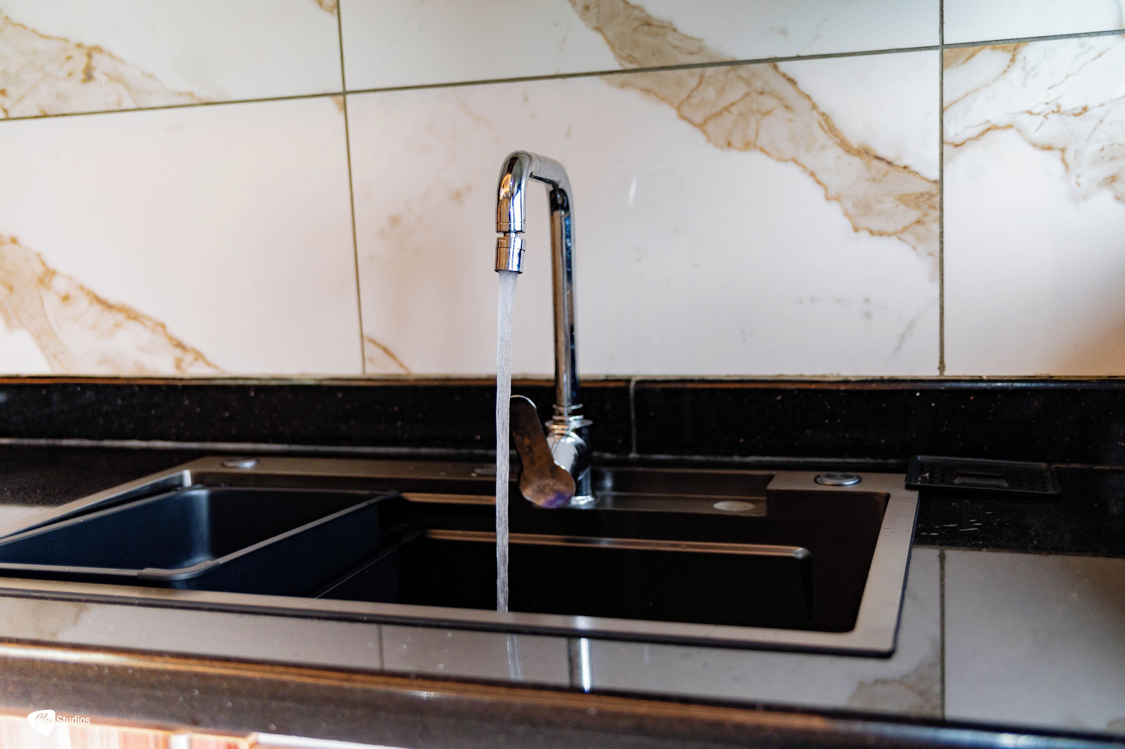 A kitchen sink with running water, a faucet, and a marble backsplash.