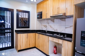 A modern kitchen with wooden cabinets, a black countertop, a microwave, and a gas stove. - Residence SOLEN (Douala)