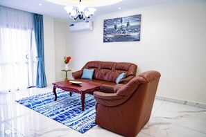 Una sala de estar con un sofá de cuero marrón, una mesa de centro de madera, un tapete azul estampado, un jarrón con flores y un cuadro en la pared.