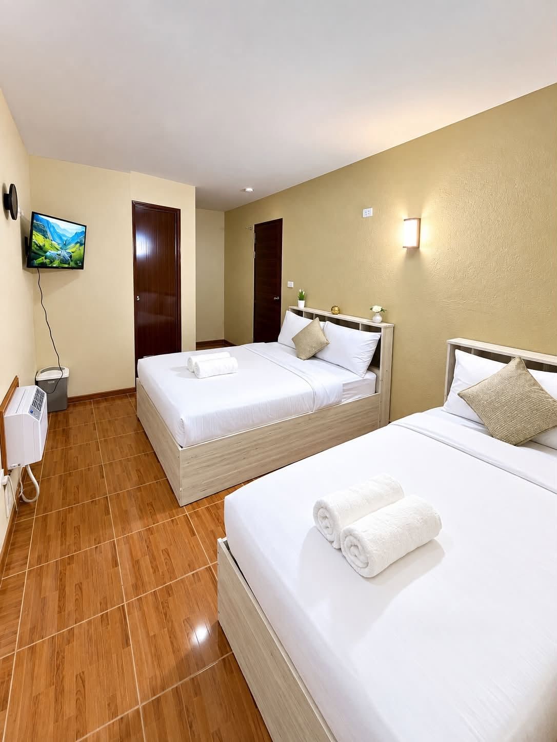Une chambre d’hôtel avec deux lits, une télévision, un radiateur et une lampe fixée au mur.