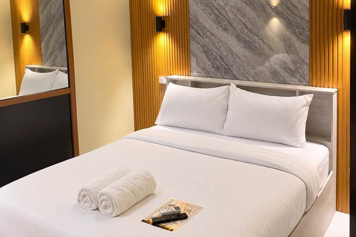 Una habitación de hotel moderna con una cama grande, un cabecero de madera, una pared decorativa de mármol y un espejo.