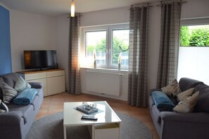 Ein Wohnzimmer mit zwei Sofas, einem Couchtisch, einem Fernseher auf einem Schrank und einem Fenster mit Vorhängen.