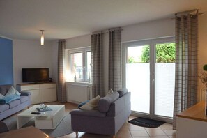 A living room with a sofa, a coffee table, a television, and a sliding glass door leading to an outdoor area. - Holiday apartment with 2 bedrooms (Horumersiel)