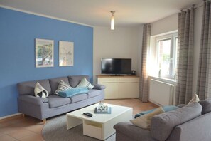 A living room with a grey sofa, a white coffee table, and a flat-screen TV on a stand. - Holiday apartment with 2 bedrooms (Horumersiel)