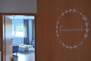 A room with a white sofa, a small table, and a window with curtains. - Holiday apartment with 2 bedrooms (Horumersiel)