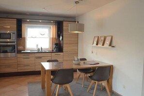 Eine moderne Küche mit integrierten Geräten, ein Essbereich mit Holztisch und Stühlen sowie ein Fenster, das natürliches Licht hereinlässt.
