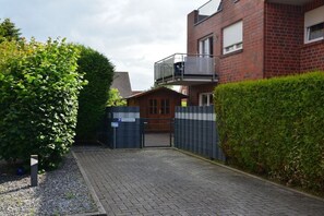 Ein Wohngebiet mit einer geschlossenen Einfahrt, die zu einem hölzernen Tor führt, ein Backsteinhaus mit Balkon und ein Heckenstreifen.