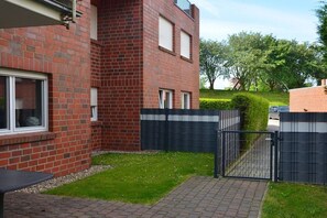A brick building with a gated entrance, a paved pathway, and a small grassy area. - Holiday apartment with 2 bedrooms (Horumersiel)
