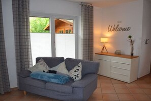 Ein Wohnzimmer mit einem grauen Sofa, einer weißen Kommode und einem 'Welcome'-Schild an der Wand.