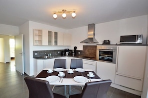 Een moderne keuken met witte kasten, een eettafel voor vier personen en een magnetron op het aanrecht.
