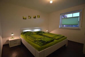 Ein Schlafzimmer mit einem Bett, Nachttischen, einem Fenster mit Jalousien und Wandbildern.
