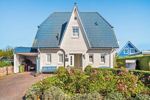 Ein zweistöckiges Haus mit einem steilen Satteldach, einer Veranda und einem gepflegten Garten mit rosa Blumen.