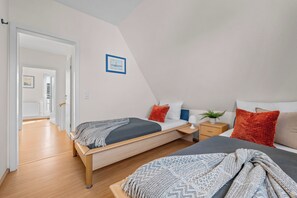 Ein modernes Schlafzimmer mit zwei Betten, einem Nachttisch, einem Topfpflanzen und einem gerahmten Bild an der Wand.