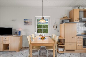 Ett modernt kök med matplats, träskåp, en inbyggd ugn och ett fönster med utsikt över grönområden.
