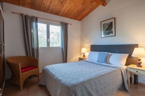 A bedroom with a bed, a chair, a nightstand, a lamp, a window with curtains, and a wall-mounted picture. - Holiday home with 3 bedrooms (Porto Vecchio)