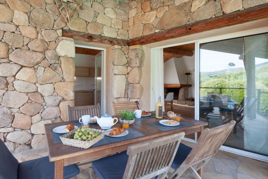 Un espace de restauration en plein air avec des murs en pierre, une table en bois dressée pour le petit-déjeuner et une vue sur le paysage.