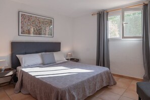Ein Schlafzimmer mit einem Bett, Nachttischen, einem Fenster mit Vorhängen und einem an der Wand hängenden Kunstwerk.