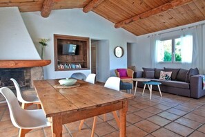 Ein gemütlicher Wohnbereich mit Holztisch, weißen Stühlen, einer Couch und einem an der Wand befestigten Fernseher.