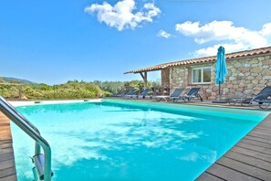 Ein Schwimmbecken mit Liegestühlen und ein Gebäude mit steinernen Mauern und einem Ziegeldach.