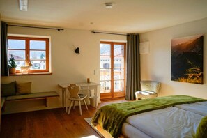 A room with a bed, a desk, a chair, and a window with a view of buildings. - Holiday home with 1 bedroom (Unterwössen)