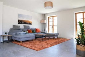A modern living room with a grey sectional sofa, a coffee table, and a large window providing natural light. - Holiday home with 1 bedroom (Unterwössen)