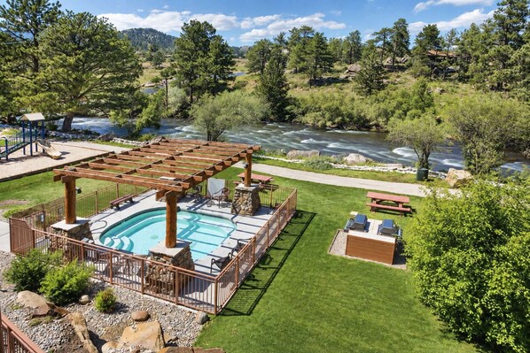 Zona de piscina con un pérgola, sillones de descanso y vistas a un río.