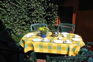 An outdoor dining area with a table set for four, surrounded by green chairs, against a backdrop of a leafy hedge. - Frisian house on Möwenweg (Norden-Norddeich)