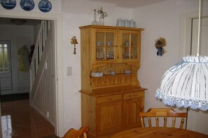 Un mueble de madera con puertas de vidrio, una mesa de comedor con sillas y un mantel de crochet.