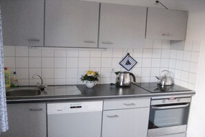 A kitchen with white cabinets, a dishwasher, a kettle, and a sink. - Frisian house on Möwenweg (Norden-Norddeich)
