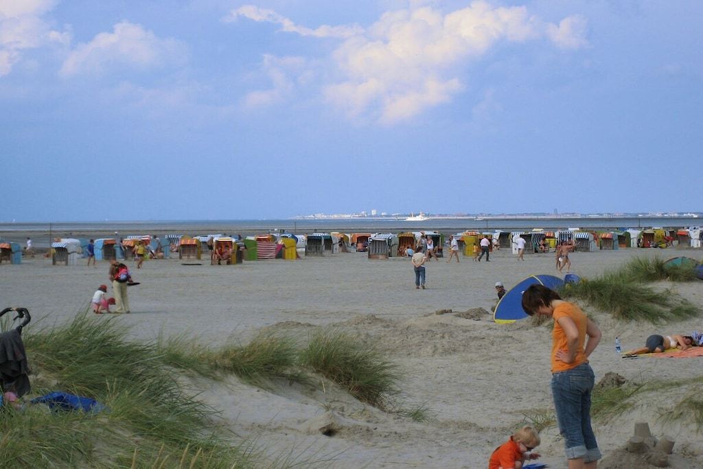 En strand med telte og mennesker, hvor nogle sidder og andre går.
