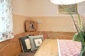Ein Eckzimmer mit einer Holzbank, einem kleinen Holzkästen, einem gemusterten Teppich und einem gerahmten Bild an der Wand.