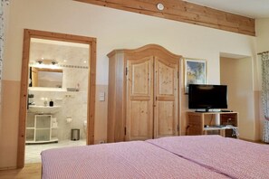 A bedroom with a bed, a wooden wardrobe, a television, and a bathroom visible through an open door. - Holiday apartment with 0 bedrooms (Fischbachau)