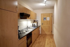 A compact kitchen with wooden cabinets, a black range hood, and a tiled backsplash. - Holiday apartment with 0 bedrooms (Fischbachau)