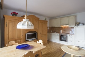 A kitchen with wooden cabinets, a dining table with chairs, a hanging light fixture, and a television. - Holiday apartment with 1 bedroom (Farchant)