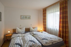 A double bed with floral bedding, bedside lamps, and a window with curtains. - Holiday apartment with 1 bedroom (Farchant)