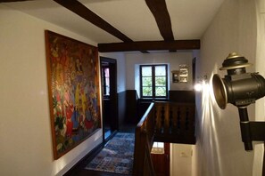 A hallway with a large painting, a staircase with a lamp, and a window with a view. - Domaine du Chasseur Wanzel (Obersteinbach)