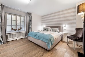 Ein Schlafzimmer mit einem Bett, einem Fenster mit Vorhängen, einer Heizung, einem Stuhl und einer Lampe.