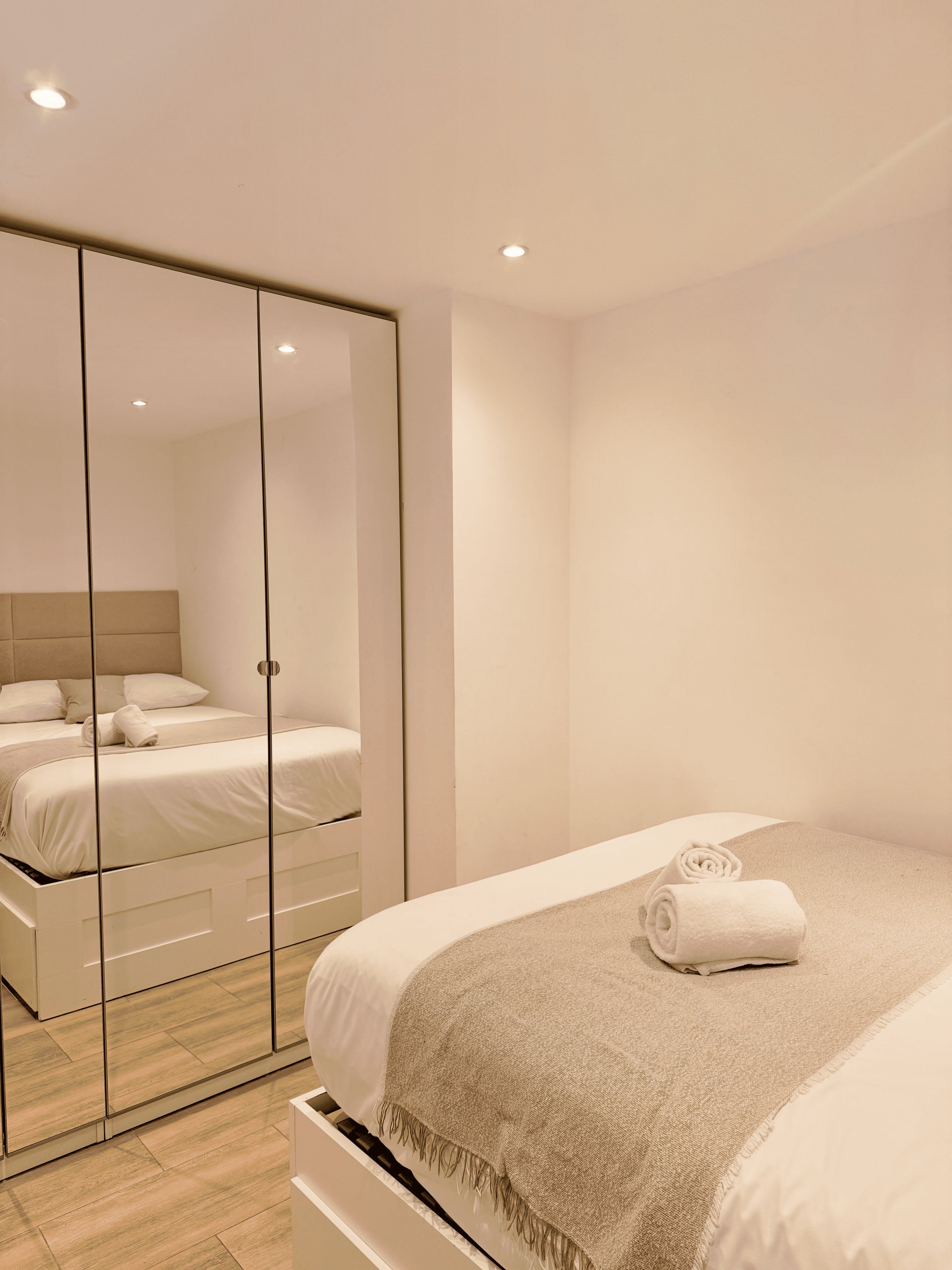 Un dormitorio moderno con un espejo grande, una cama con una toalla enrollada y un armario con puertas correderas.